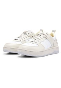 Ett par beige och vita låga sneakers med snörningsdesign och texturerade gummisulor, placerade sida vid sida på en vit bakgrund.