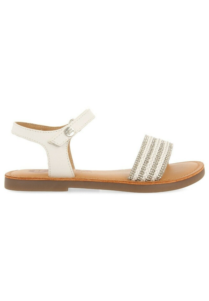 Sandalia de cuero blanca con suela plana, que presenta una tira delgada en el tobillo y un empeine ancho con adornos a rayas plateadas y blancas.