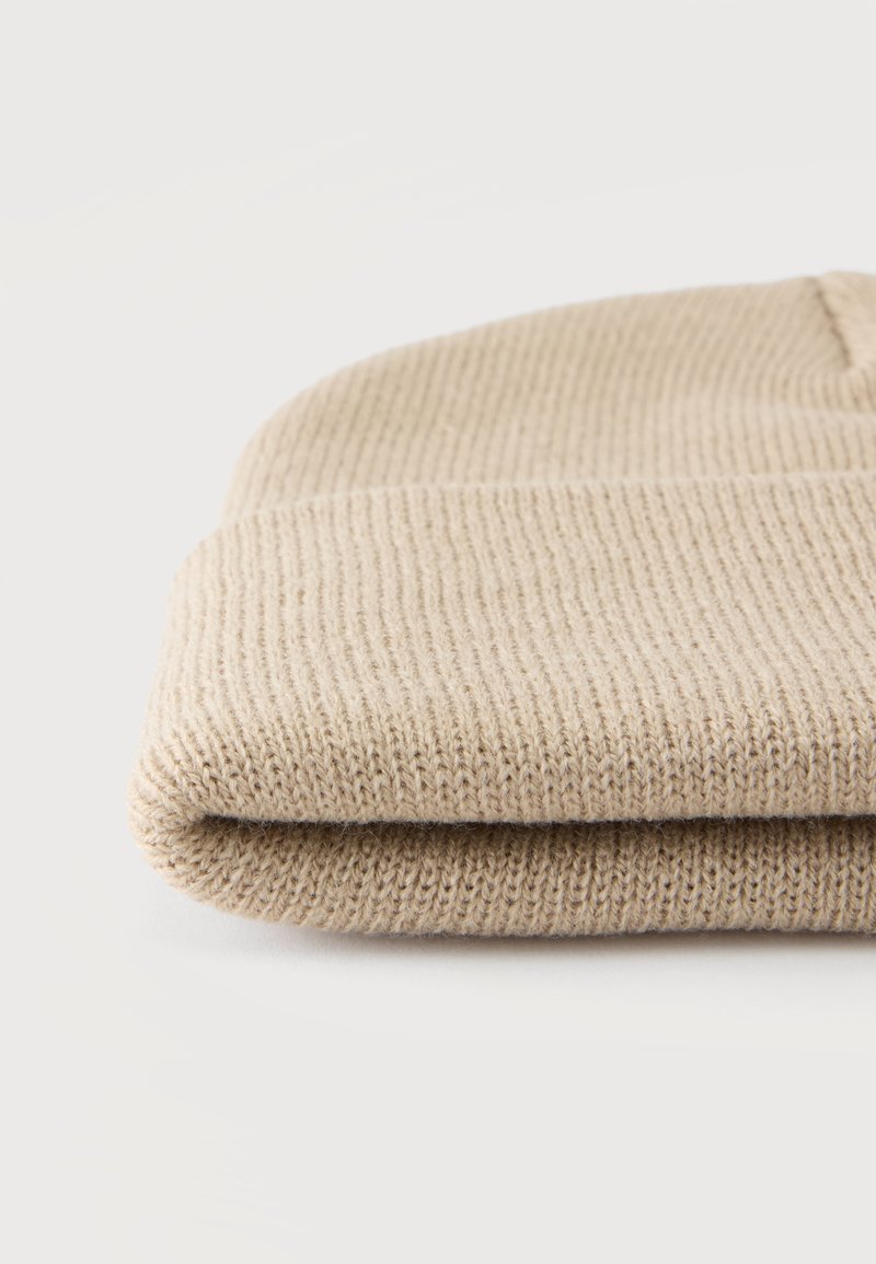 Bonnet en tricot beige plié avec texture côtelée sur fond blanc uni.