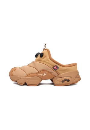 Beiger Slip-On-Sneaker mit sechseckigem Profil, Zuglasche und schwarzem Drehverschluss vor weißem Hintergrund, linke Seitenansicht.