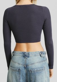 Top corto a coste blu navy con maniche lunghe, abbinato a jeans in denim azzurri a vita alta con due tasche posteriori e cuciture decorative.