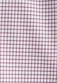 Tissu tissé présentant un motif en quadrillage avec de petits carreaux rouges et blancs, créant un aspect texturé. La surface est lisse et homogène.