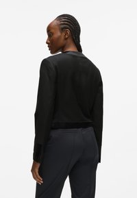 Fekete cropped blézer sima textúrával, testre szabott fazonnal és egy gombos záródással. Kiemelkedik az elegáns, minimalista dizájnjával és feddett hajtókáival.