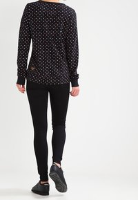 Camiseta de manga larga negra con lunares multicolores, combinada con leggins negros y zapatillas negras. Presenta un parche con el logo en la parte posterior.
