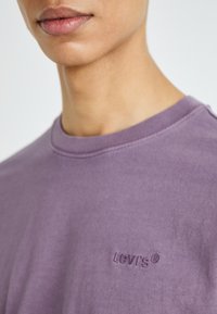 Violets kokvilnas krekls ar apaļu kaklu, kurā iespiests Levi's logo uz krūtīm. Audumam ir gluda tekstūra ar minimālu šuvju detaļu.
