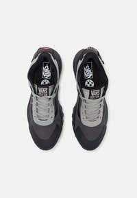 Scarpe da ginnastica grigie e nere con una tomaia testurizzata, linguetta imbottita e lacci. Presentano un logo prominente sulla linguetta e sulla soletta.