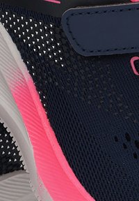 Primer plano de una zapatilla deportiva en azul marino y rosa que muestra la parte superior de malla texturizada, la entresuela rosa y parte de una correa de velcro.
