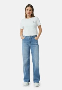 Witte katoenen t-shirt met korte mouwen en een klein logo op de borst, gecombineerd met lichtblauwe wijde jeans en witte sneakers.