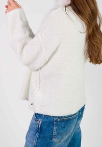 Biała, puszysta sweter z teksturowanej powierzchni, z długimi rękawami i luźnym krojem, połączony z niebieskimi dżinsami.