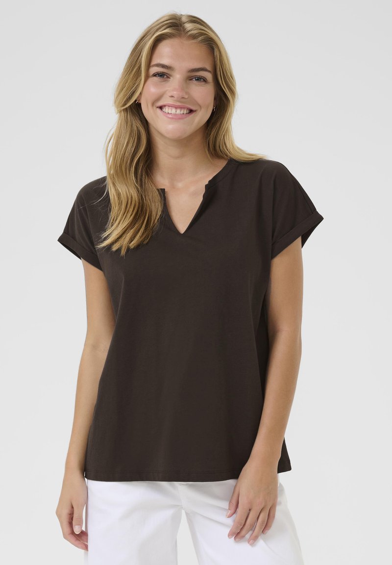 Brown short-sleeve top with a V-neck and rolled cuffs, made of soft fabric, paired with white pants, displayed against a light background.