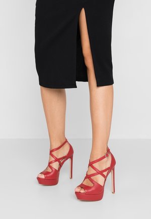 Czerwone sandały na wysokim obcasie z platformą, z krzyżującymi się paskami i odkrytą palcem. Gładka skórzana tekstura z błyszczącym wykończeniem oraz smukłe szpilki.