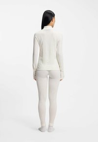 Biała bluzka z długim rękawem i wysokim kołnierzem o teksturowanym wzorze w romby, zestawiona z dopasowanymi białymi legginsami z żebrowanymi detalami i gładkim wykończeniem.