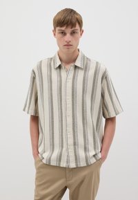 Camicia a maniche corte con bottoni di colore beige con strisce verticali verdi e nere. Realizzata in tessuto testurizzato, presenta un colletto e una vestibilità rilassata.