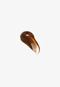 Prodotto marrone simile a una crema, con una consistenza liscia e lucida, che forma una forma a goccia con una striscia più chiara lungo un bordo.