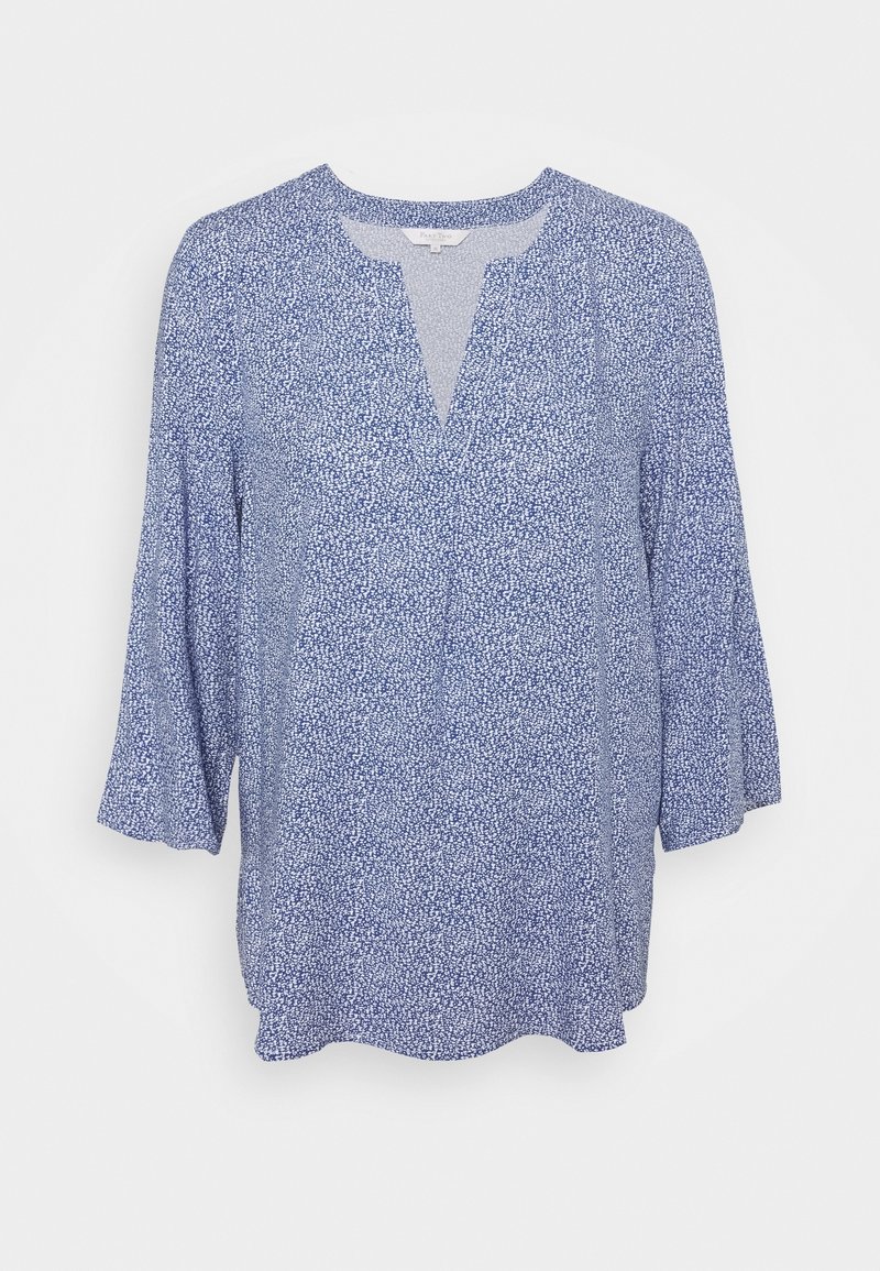 Blouse bleu et blanc à pois, avec des manches cloche trois-quarts et un col rond fendu, présentée sur un fond blanc.