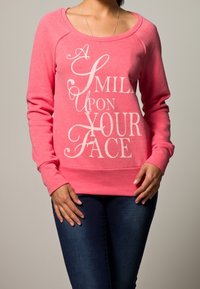Roze sweatshirt met een ronde hals en raglanmouwen, met witte tekst die zegt "EEN LAKENS OP UW GEZICHT." Zachte stoftextuur.