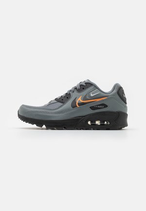 Szaro-czarny sneaker Nike Air Max z pomarańczowymi i białymi logo Swoosh oraz widoczną poduszką powietrzną w podeszwie, widok z boku na białym tle.