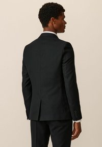 Chaqueta de traje negra con una abertura centrada en la parte posterior, solapas estriadas y tres botones en cada puño. Acabado de tela suave.