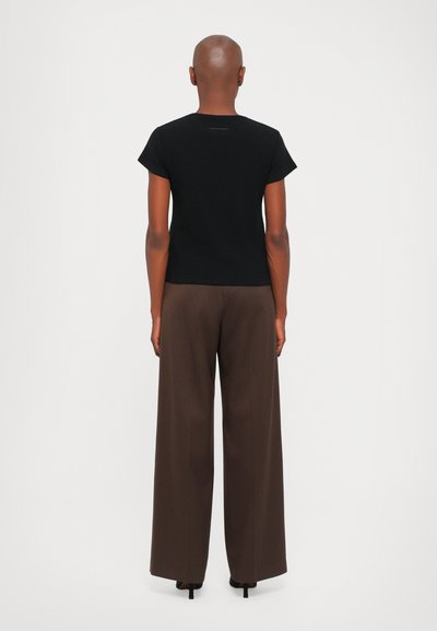 Black short-sleeve t-shirt made of cotton, paired with wide brown trousers. T-shirt features a subtle seam detail at the neckline.