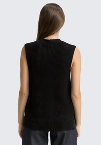 Schwarzer ärmelloser Strickpullover mit geriffelter Struktur. Verfügt über einen hohen Halsausschnitt und einen längeren Saum hinten, gefertigt aus einem weichen Stoff.