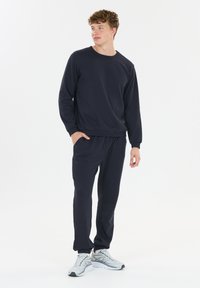 Marineblauwe sweatshirt en bijpassende joggers van zacht materiaal, met lange mouwen, elastische boorden en een ontspannen pasvorm. Casual sportieve schoenen.