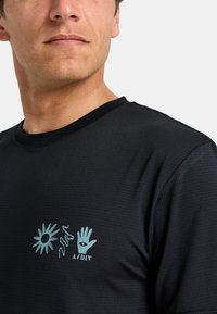 Camiseta negra de manga corta con una superficie texturizada. Presenta un diseño gráfico en azul claro de un sol, una línea y una mano en el lado izquierdo del pecho.
