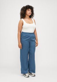 Blå vida byxor med elastisk midja, kombinerat med en vit tanktop med fyrkantig halsringning, som bärs med flerfärgade sneakers.