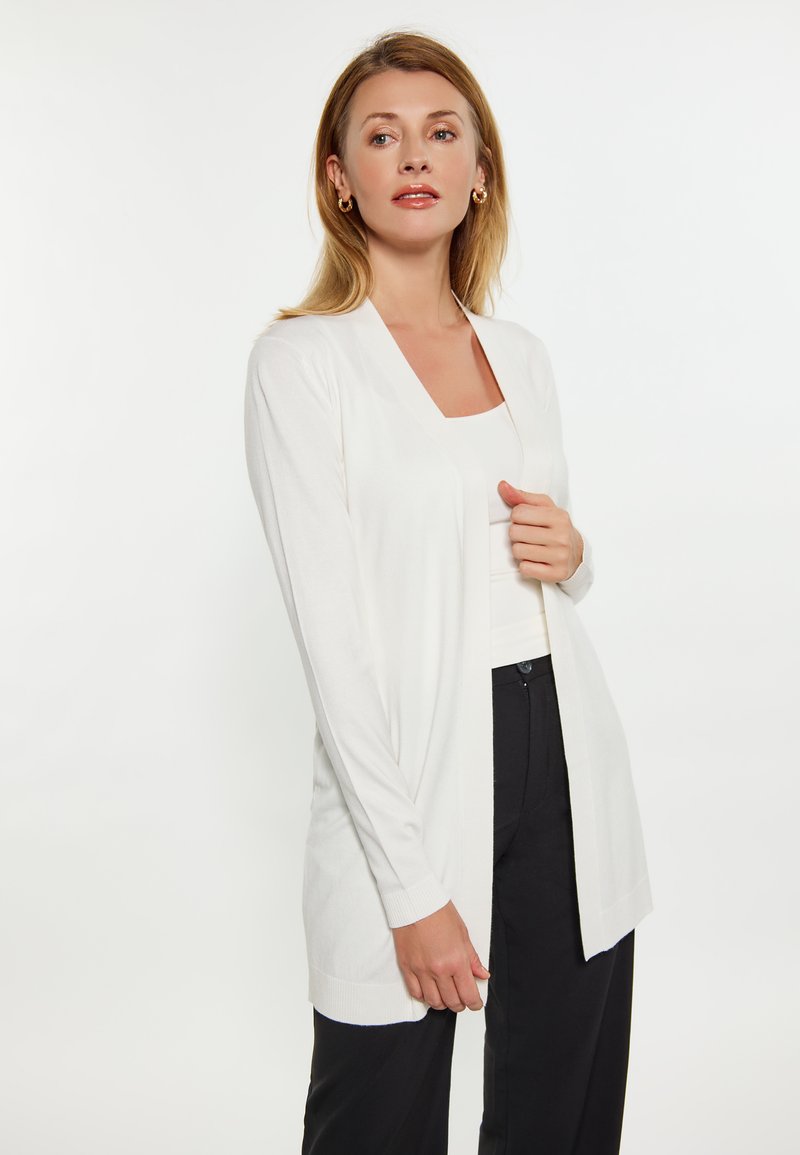 Witte cardigan met lange mouwen en een open voorkant, zachte textuur, geribbelde manchetten en een ontspannen pasvorm, gecombineerd met een zwarte onderkant.