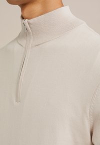 Bežna pulover z napol dolgim zadrgo, ki se ponaša z rebrastim ovratnikom in gladko teksturo, strukturiranimi šivi in prilegajočim krojem.