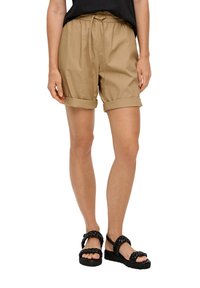 Khaki szorty z marszczoną talią i sznurkiem, z podwiniętymi mankietami. Noszone z czarnymi splecionymi sandałami na neutralnym tle.