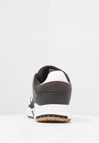 Černá sportovní bota s texturovaným svrškem, polstrovaným límcem, bílým akcentem a gumovou podrážkou s dezénem v barvě gumy.