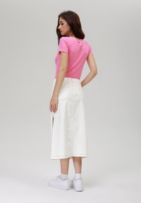 Haut rose à manches courtes côtelé avec un col scallopé, associé à une jupe en denim blanche avec une fente sur le côté, et des baskets blanches.