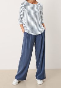 Camicia a righe con linee blu navy e bianche, scollo rotondo e maniche 3/4 abbinata a pantaloni larghi blu navy e sneakers bianche.