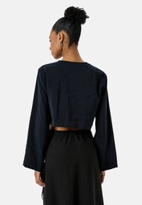 Czarny top o kroju cropped z długimi rękawami, lekko teksturowany materiał, okrągły dekolt. Posiada wycięcie na plecach, w zestawie ze spódnicą.