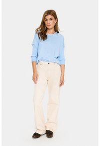 Pullover leggero blu con una vestibilità morbida, abbinato a jeans crema a vita alta. Scarpe marroni e gioielli semplici completano l'outfit.