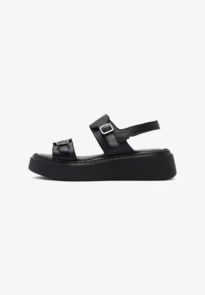 Black leather platform sandals featuring dual straps with buckle accents, a flat sole, and a textured insole for added comfort.