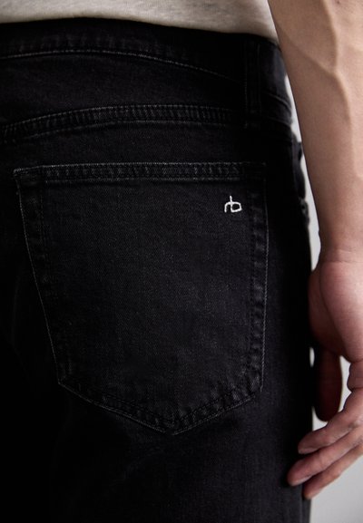 Jeans de mezclilla negra con un bolsillo trasero que presenta un logo blanco. La tela tiene una textura suave y un diseño clásico de cinco bolsillos.