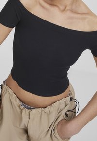 Black ribbed off-the-shoulder crop top with short sleeves, paired with beige drawstring pants featuring side pockets and a relaxed fit.