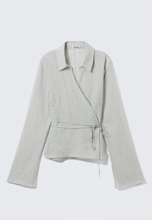 Chemisier léger gris clair avec un col, des manches longues, des rayures subtiles et un détail de taille nouée. Fabriqué dans un tissu texturé.