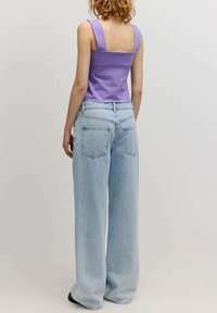 Lila mouwloze top met brede bandjes, gecombineerd met hooggewaadde, lichtblauwe wijde jeans. Bevat een vierkante rug en denimzakken.
