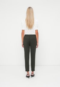 Vit broderad blus med puffiga korta ärmar, matchad med mörkgröna skräddarsydda byxor i ankellängd och svarta klackskor.