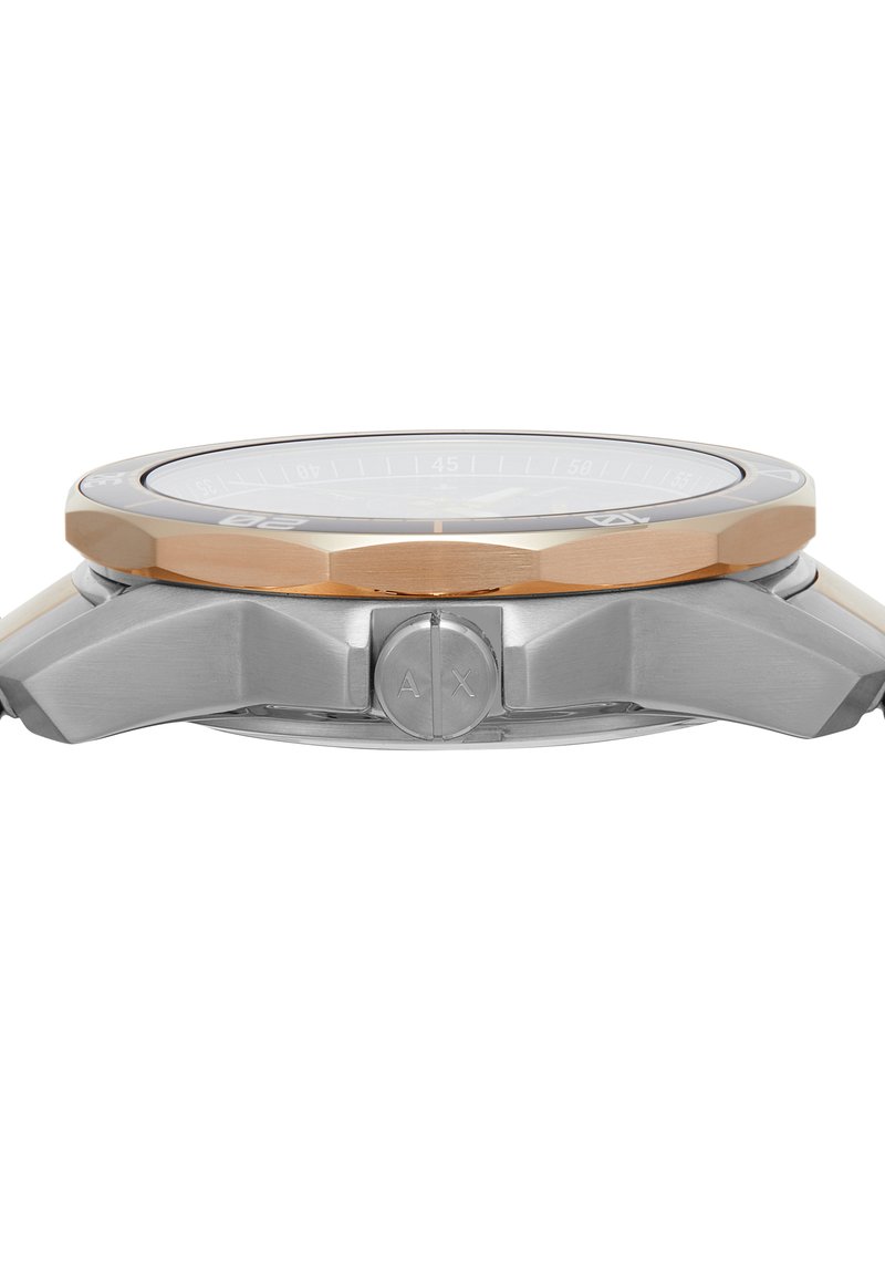 Vue de côté d'une montre-bracelet en argent et or rose avec une lunette striée et "AX" gravé sur le bouton de la couronne.