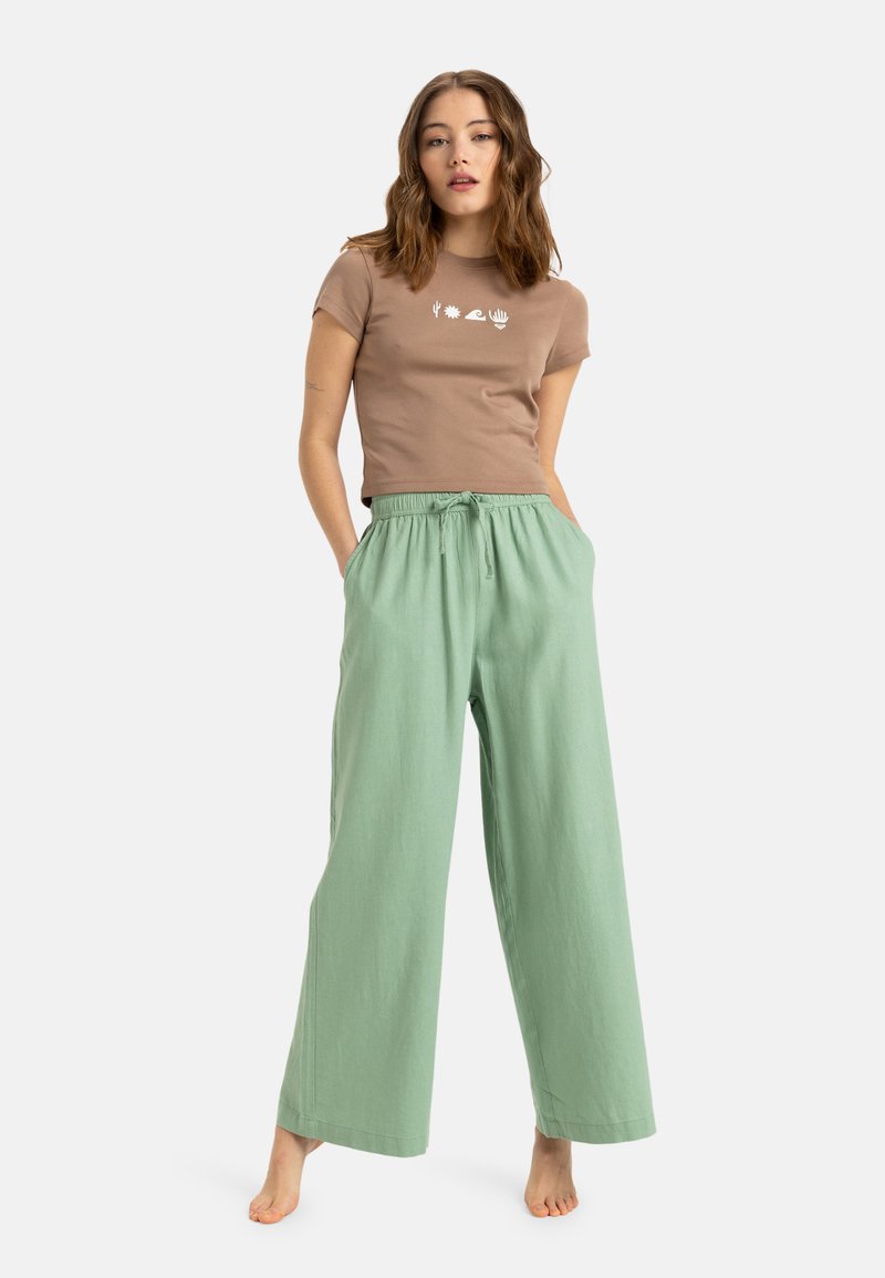 T-shirt brun à manches courtes avec des motifs graphiques blancs et un pantalon large vert clair avec une taille élastique et des poches avant.
