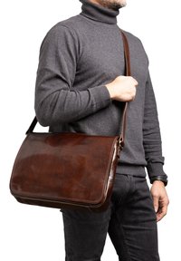 Borsa messenger in pelle marrone con texture liscia, forma rettangolare e tracolla regolabile, portata a tracolla.