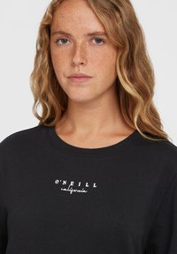 Mustra musta dress with klassikalise mehe kaela, millel on rindkerel valged tähed "O'Neill California". Kangas tundub pehme ja kergelt tekstureeritud.
