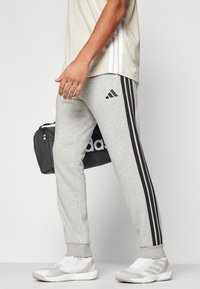 Hallide hallid mustade külgtriipudega, ribastatud sääreotsadega ja Adidas logo. Kombineeritud heleda särgi ja valgete/hõbedaste spordijalkadega.