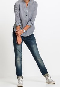 Camisa de botones a rayas en azul y blanco, combinada con jeans de mezclilla oscuros. Las zapatillas son grises con acentos blancos; el reloj es de plata con una esfera redonda.