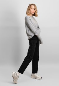Maglione grigio con spalle scese, pantaloni neri e sneaker bianche. Il maglione ha una texture morbida; i pantaloni sono di stile dritto.