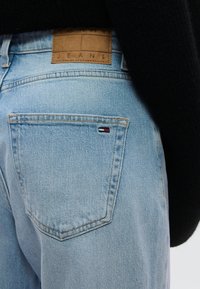 Φωτεινό γαλάζιο τζιν παντελόνι με δερμάτινο πίσω ταμπελάκι που γράφει "TOMMY JEANS", με μια μικρή λεπτομέρεια σε κόκκινο, άσπρο και μπλε στην τσέπη.