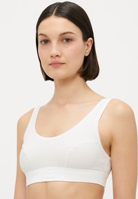 Hvit bomullsbralette med scoop-hals, brede stropper og sømløse sider. Inkluderer en brodert logodetalj på elastikken.